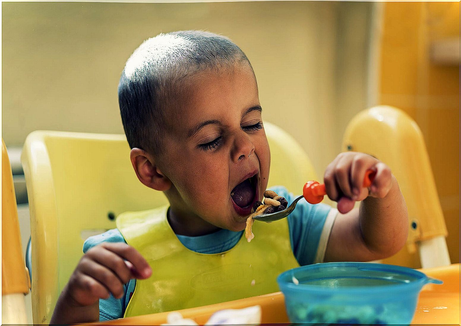 Boy between 2 and 3 years old eating with a spoon by himself.