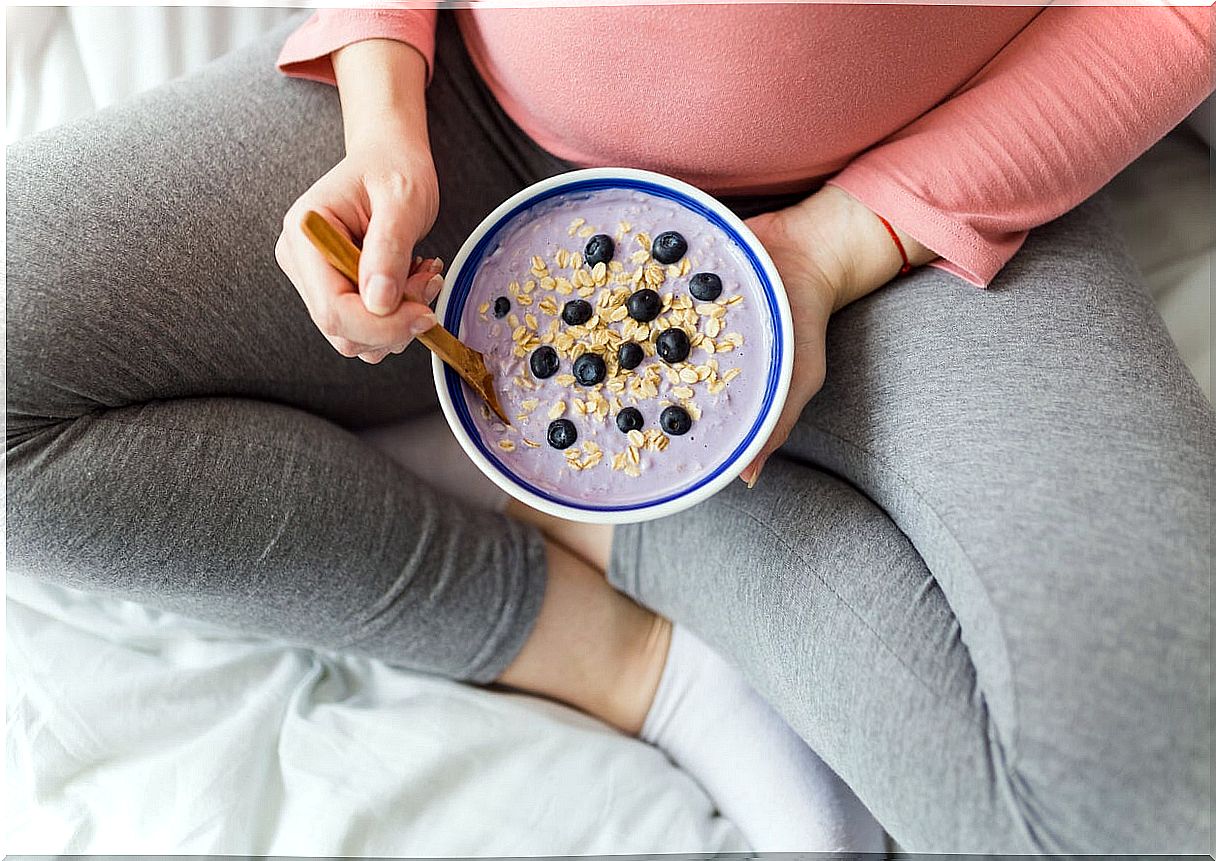 Pregnant woman eating yogurt with cereals and fruit.