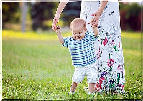 Baby taking his first steps holding his mother's hands.